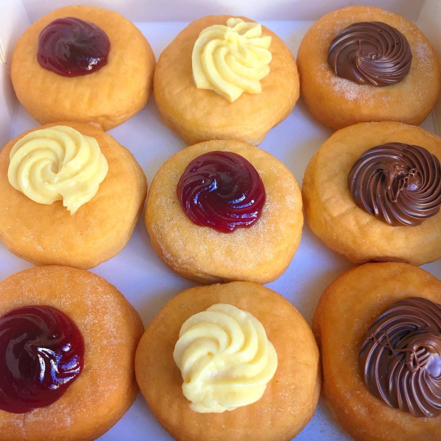 Nine golden donuts topped with swirls of red jam, yellow custard, and chocolate spread.