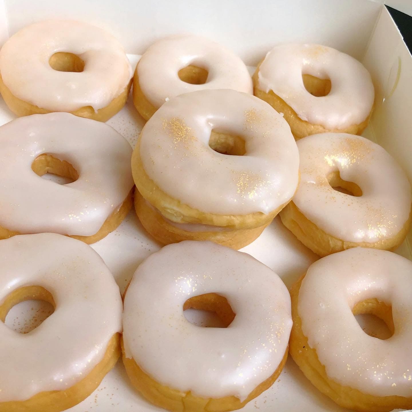 Box of ten golden donuts with glossy white icing and shimmering gold glitter dust.